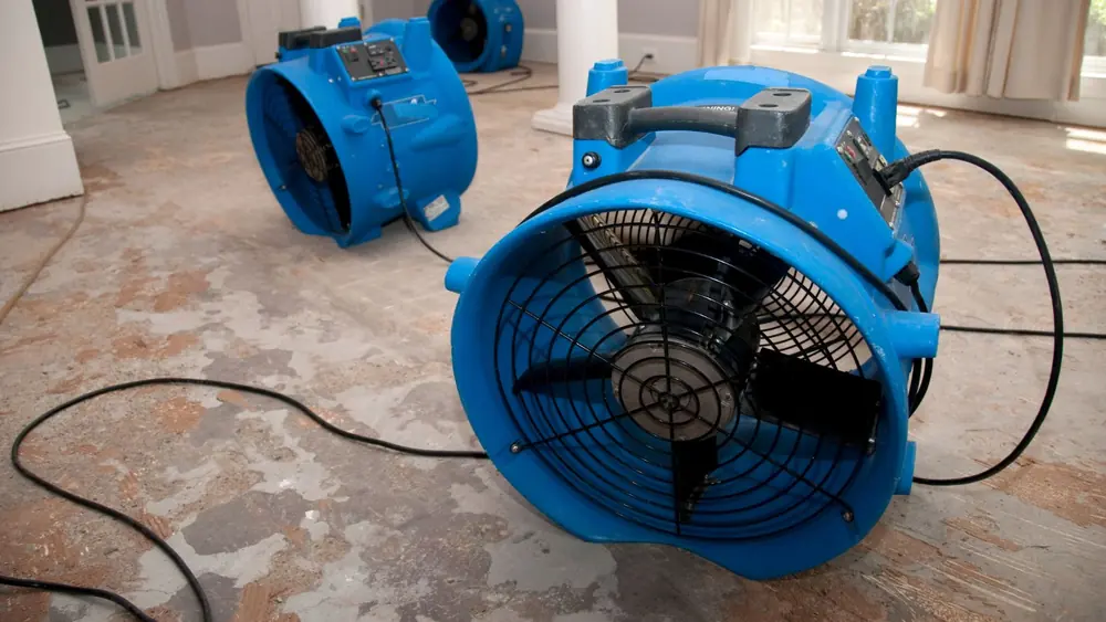 Blue air mover running on a damp floor to dry the structure